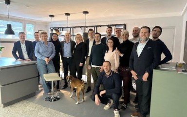 Gruppe von Geschäftsleuten mit Hund posiert lächelnd in modernem, hellen Bürobereich.