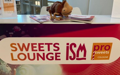 Messestand mit Aufschrift „Sweets Lounge ISM“, Prospekten und gehäkeltem Chamäleon auf dem Tresen.