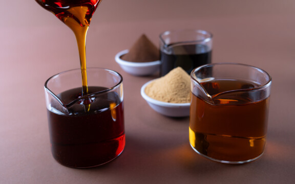 Dunkler Sirup wird in Glasbecher gegossen, daneben weitere Becher und Pulverschalen.