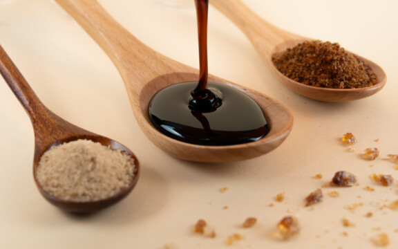 Drei Holzlöffel mit hellbraunem Zucker, dunklem Sirup und braunem Zucker, nah aufgenommen.