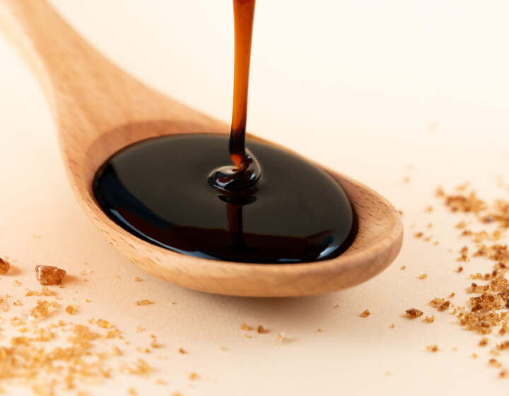 Dunkler Sirup fließt in einen Holzlöffel, umgeben von verstreutem braunem Zucker.