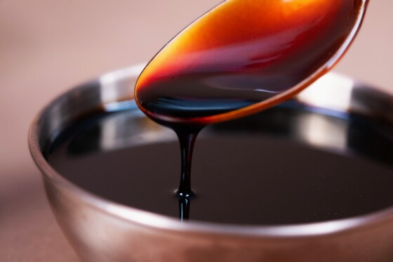 Nahaufnahme eines Löffels, aus dem dunkelbraune, sirupartige Flüssigkeit in Schale tropft.
