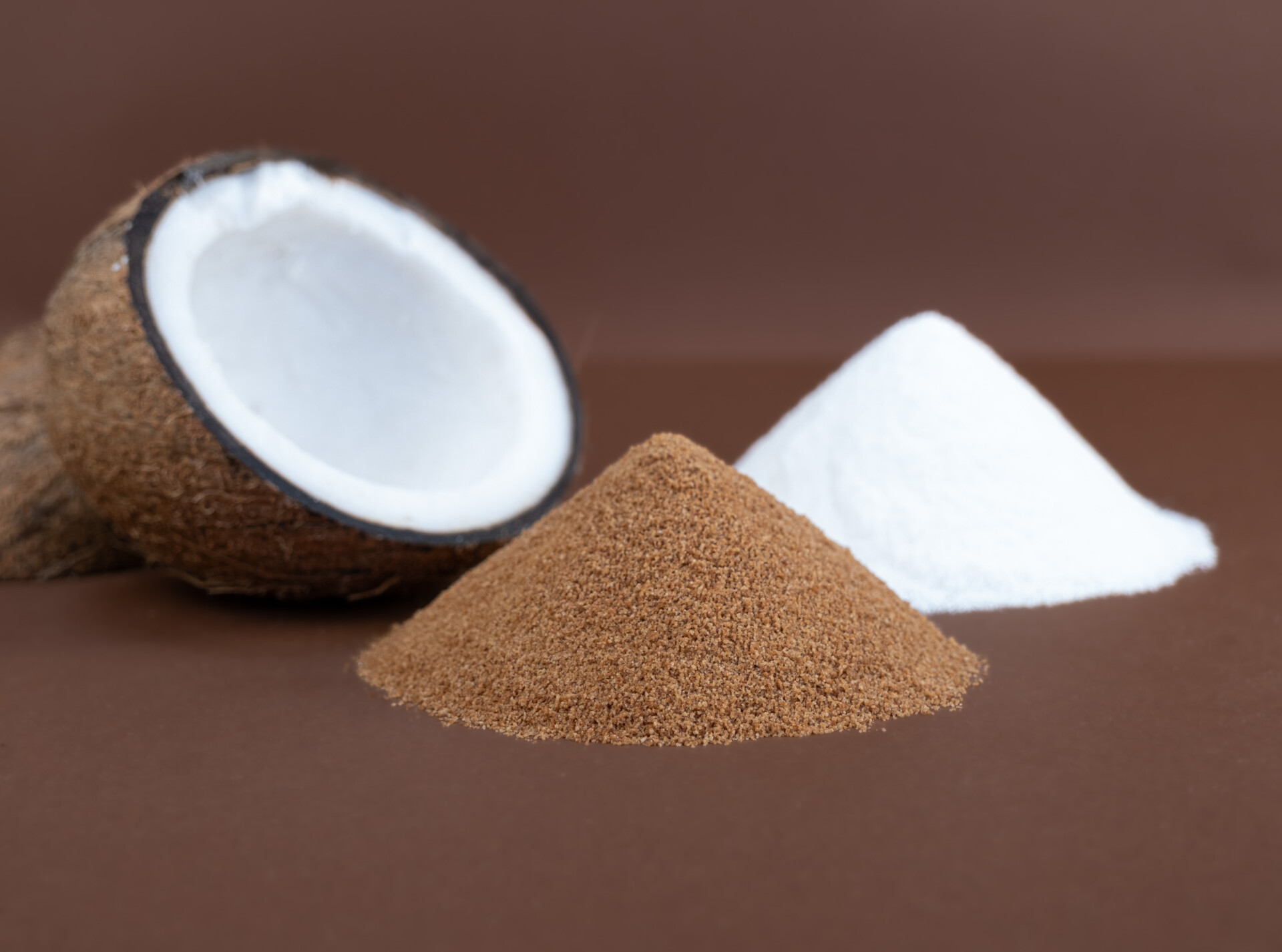 Halbe Kokosnuss neben braunem und weißem Pulverhaufen auf braunem Hintergrund arrangiert.