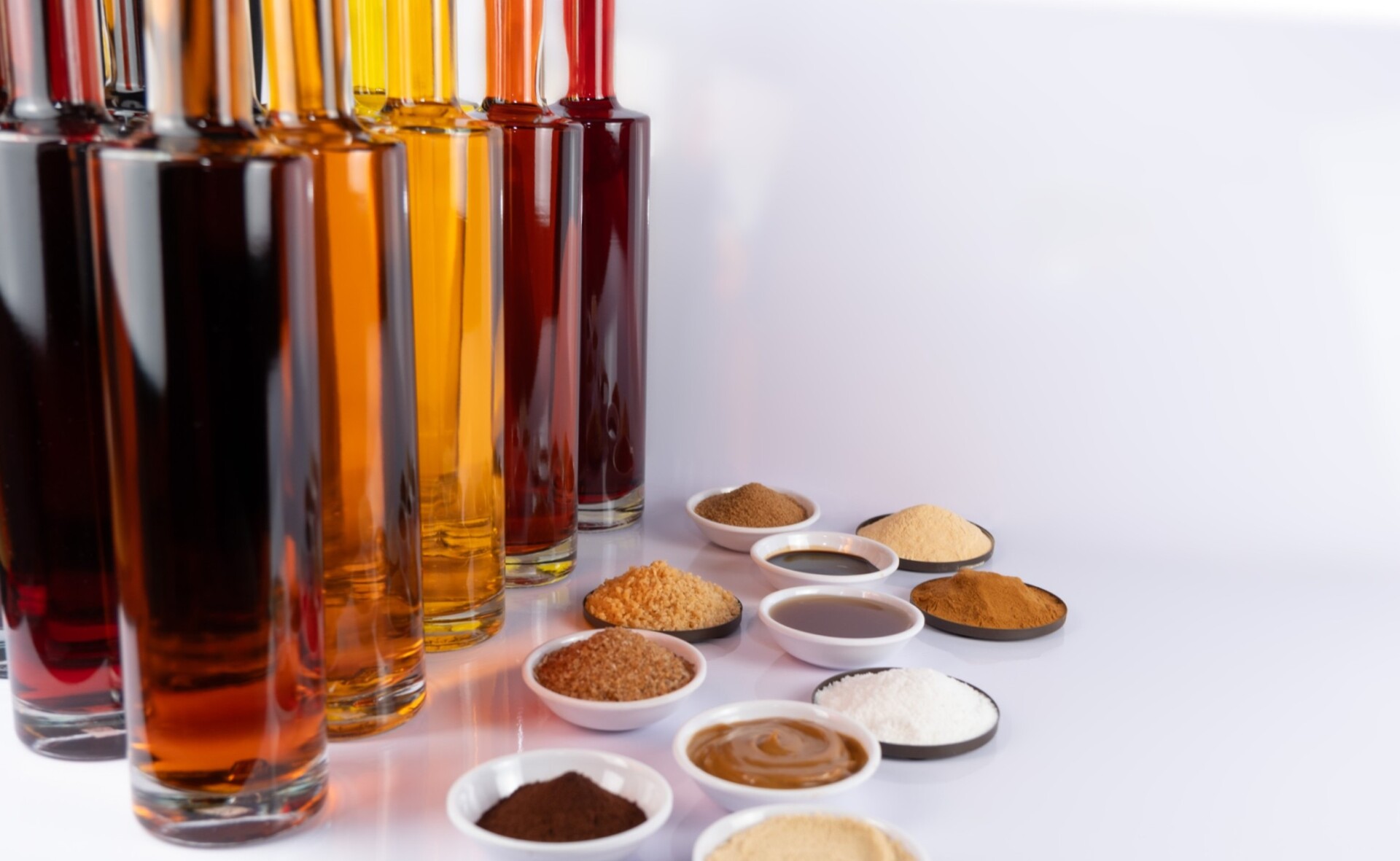 Reihe bunter Glasflaschen mit Flüssigkeiten neben Schälchen mit verschiedenen Pulvern und Soßen.